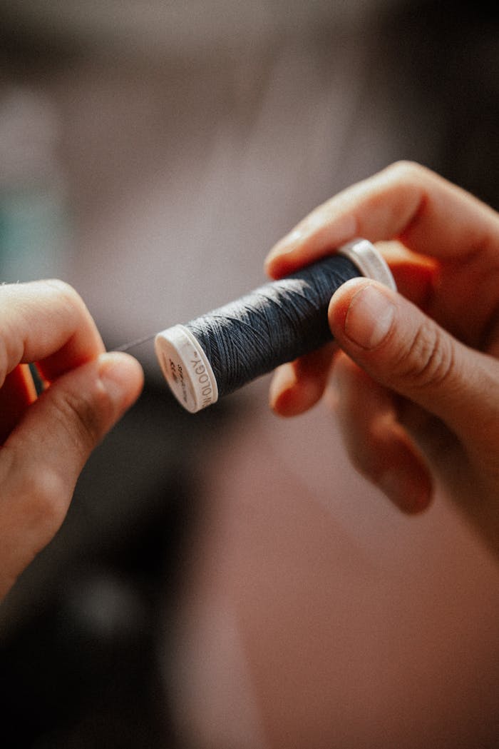 Detailed image showing hands holding a blue thread spool, highlighting crafting or sewing concepts.