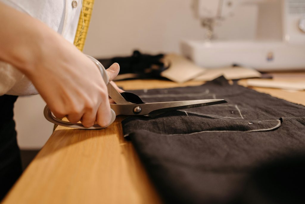 A seamstress cuts black fabric with scissors, showcasing tailoring expertise.