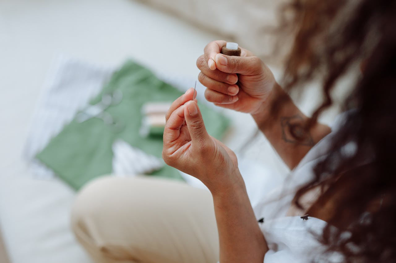Close-up of a woman's hands threading a needle with fabric in the background. Perfect for sewing and crafting themes.