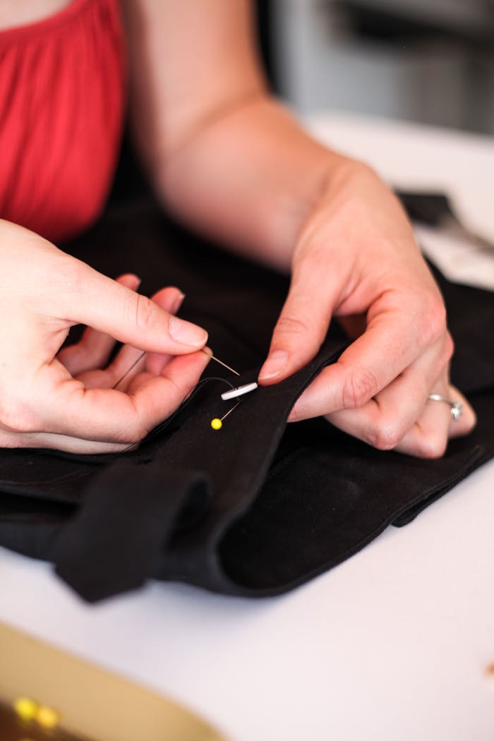 Hands sewing black fabric with needle and pin, showcasing detailed craftsmanship.